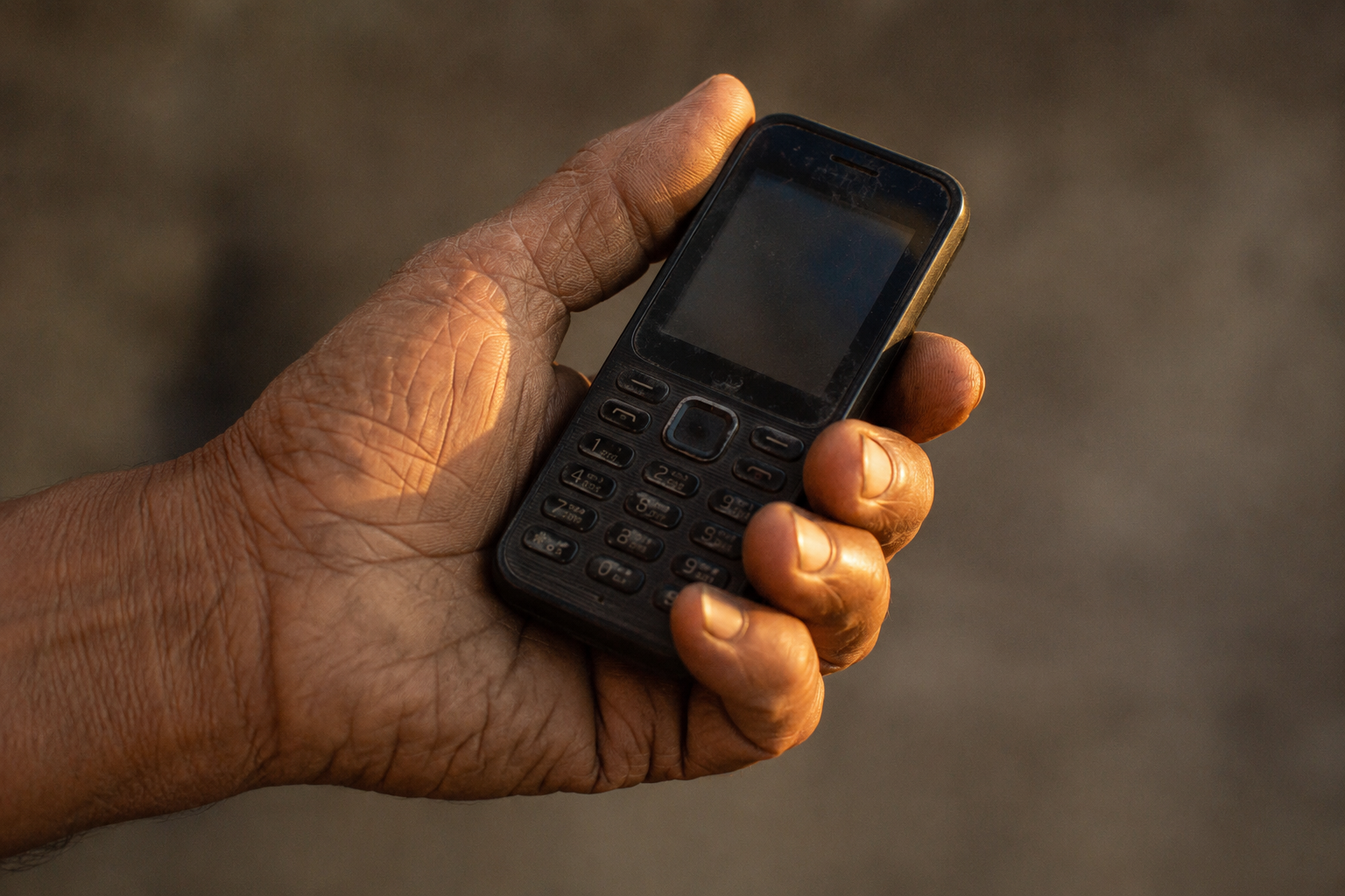Is Bitcoin too complicated to use? A hand holding a basic feature phone in warm light